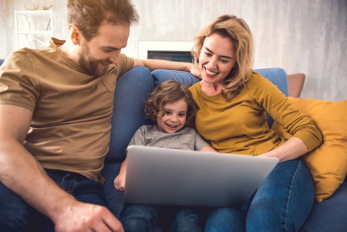 Eltern und Kind sitzen vor einem Laptop und buchen online eine Reise