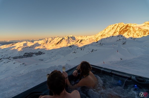 Två personer i bubbelpool med utsikt över snöklädda berg.
