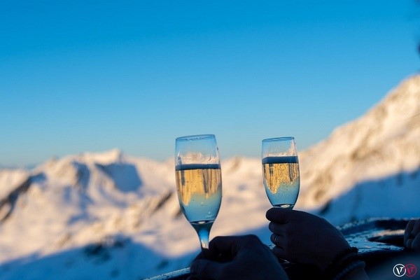 Två glas höjs med Alperna i bakgrunden.