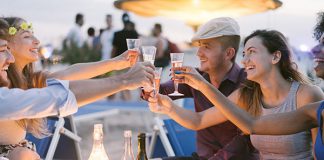 Een groepsreis boeken, hoe werkt dat? Een groep vrienden in een strandtent proosten met elkaar.