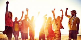 Top 4 bestemmingen voor een groepsreis Groep jonge mensen op het strand met armen in de lucht.