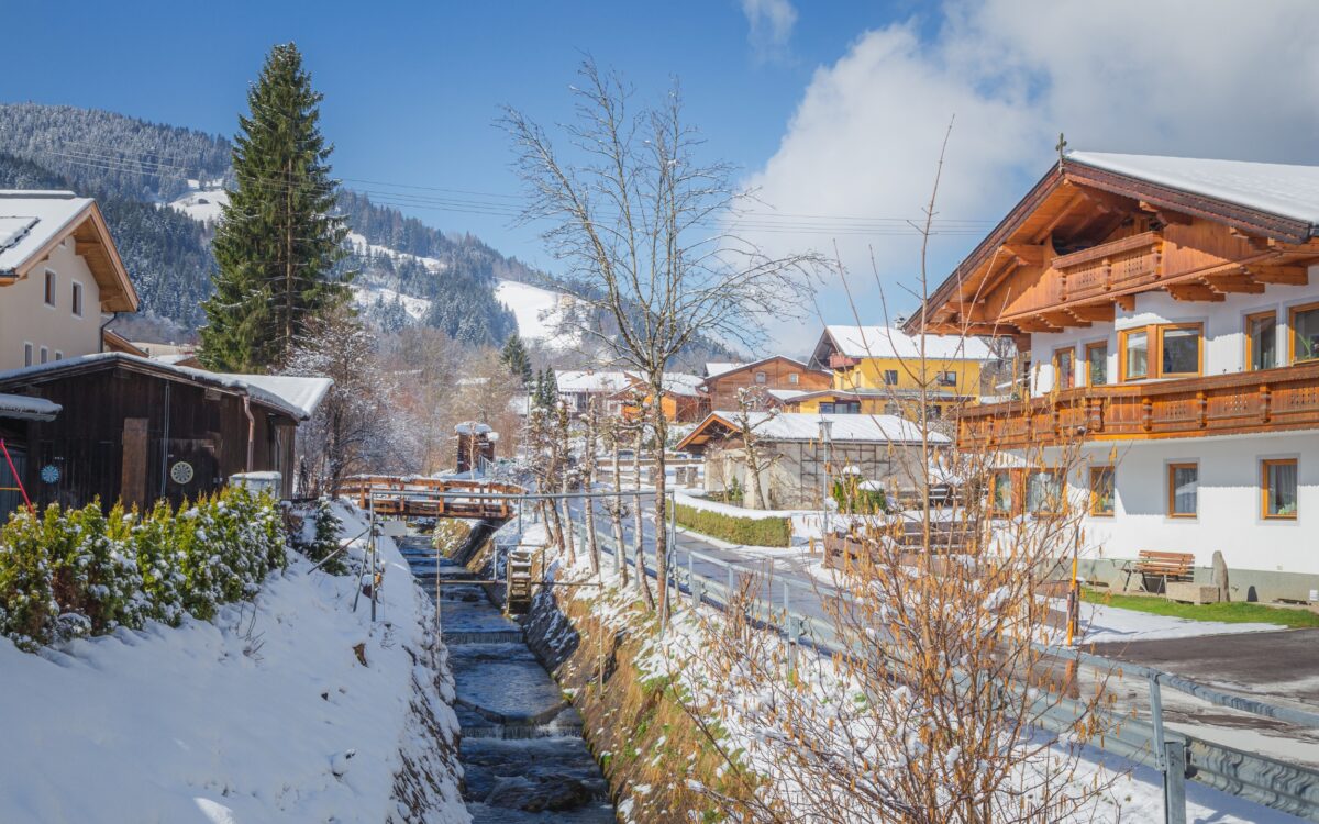 Eine Straße und verschneite Chalets in der Wildschönau. Die Sonne scheint.