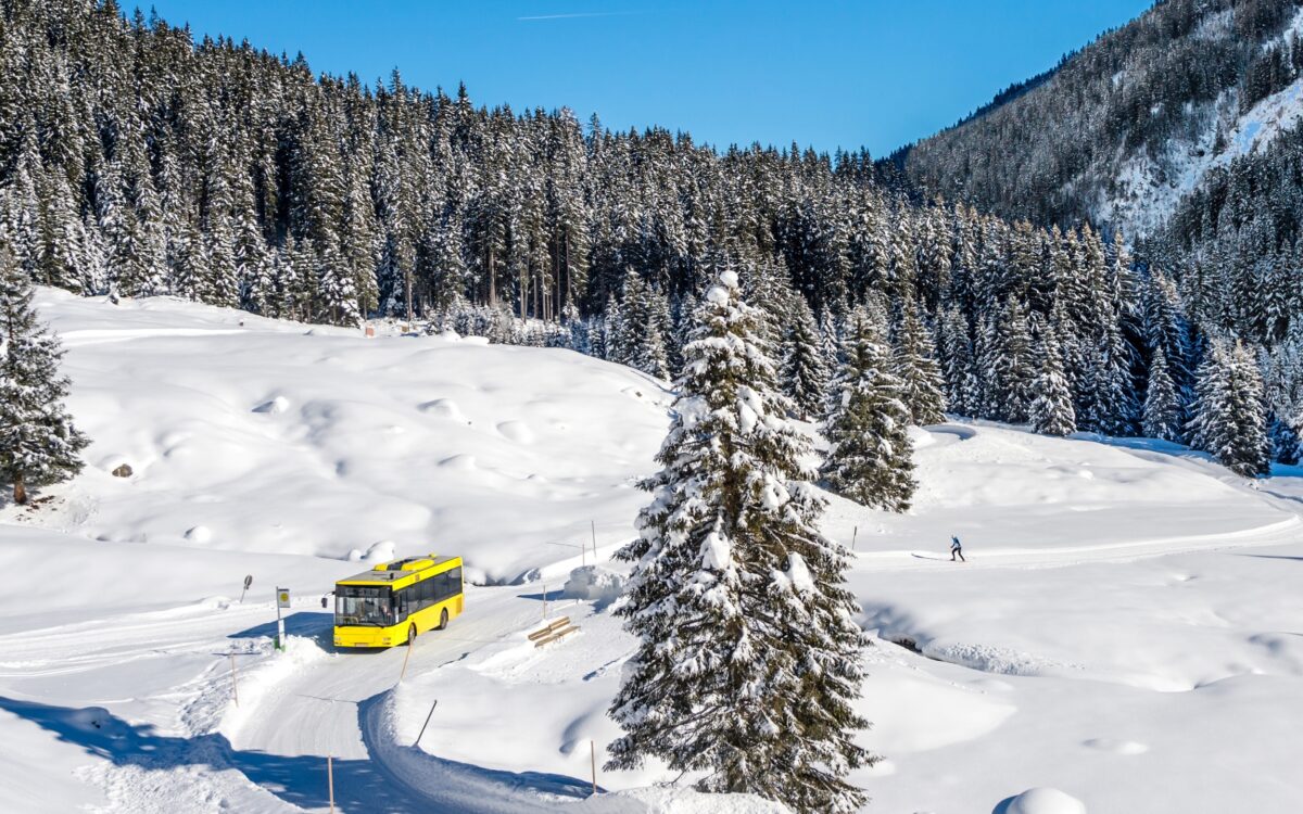 Ein gelber Bus auf einer verschneiten Landstraße.