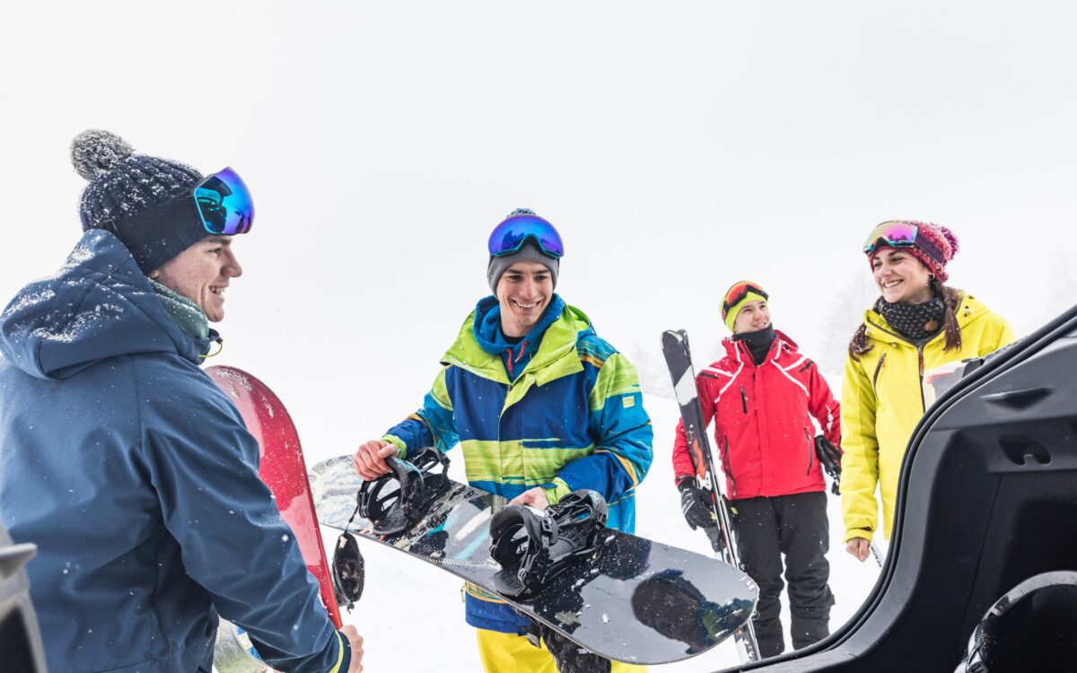 Ein Gruppe von vier jungen Menschen, die mit Snowboards und Skiern im Schnee stehen.