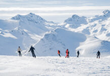 Eine Gruppe von Menschen, die auf Skiern oder Snowboard eine Skipiste in den Alpen hinunterfahren.