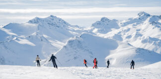 Eine Gruppe von Menschen, die auf Skiern oder Snowboard eine Skipiste in den Alpen hinunterfahren.