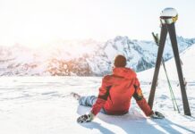 Erwachsener Mann genießt den Sonnenuntergang mit Skiausrüstung neben sich