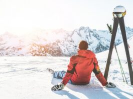 Erwachsener Mann genießt den Sonnenuntergang mit Skiausrüstung neben sich