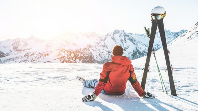 Erwachsener Mann genießt den Sonnenuntergang mit Skiausrüstung neben sich